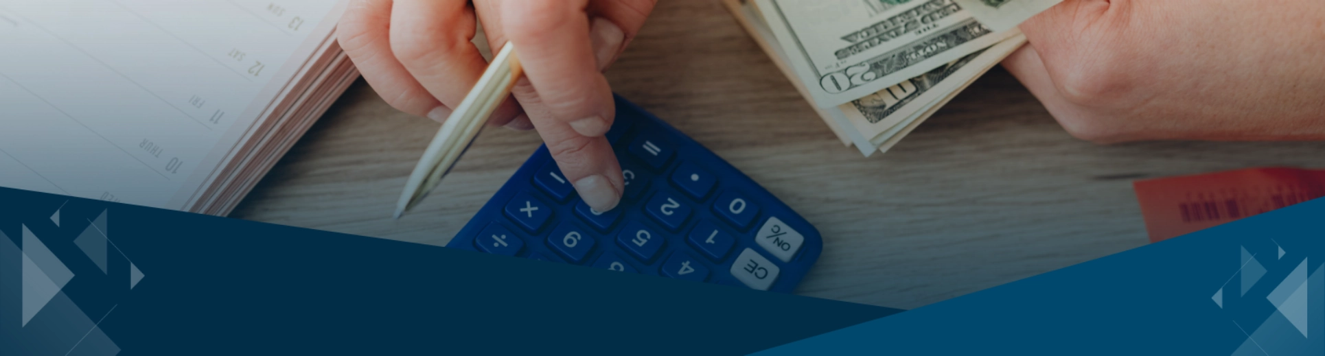 Person using a calculator with a stack of cash on a desk
